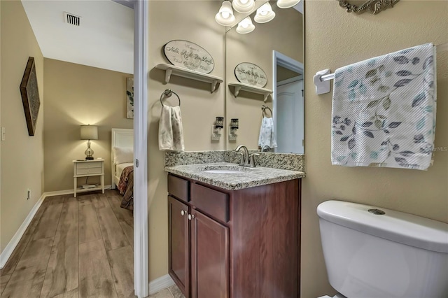 bathroom with vanity, toilet, baseboards, wood finished floors, and visible vents