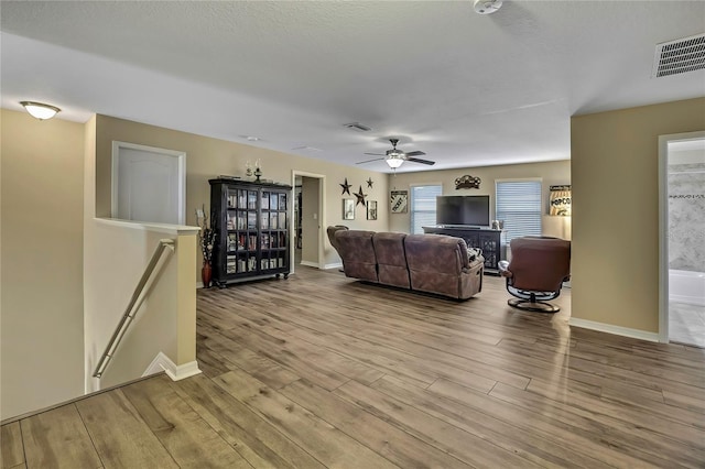 living room with baseboards, ceiling fan, wood finished floors, and visible vents