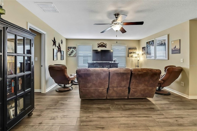living area featuring visible vents, baseboards, ceiling fan, and wood finished floors