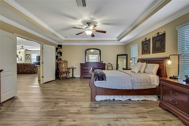 bedroom featuring ornamental molding, a tray ceiling, wood finished floors, and visible vents