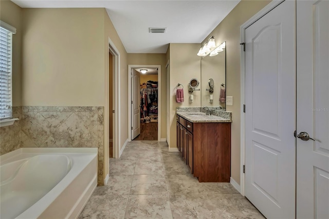 full bathroom featuring visible vents, vanity, baseboards, a walk in closet, and a bath