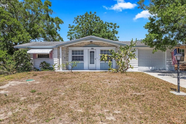 single story home with an attached garage, stone siding, a front yard, and concrete driveway