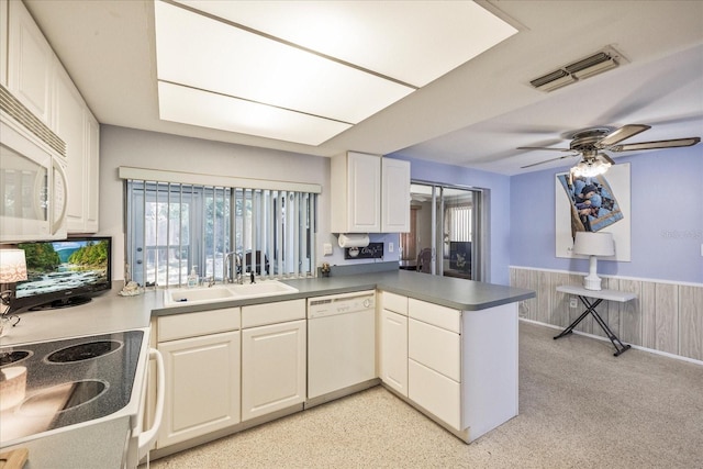 kitchen featuring visible vents, a peninsula, white appliances, ceiling fan, and a sink