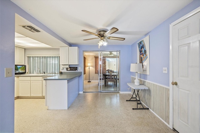 kitchen featuring a ceiling fan, visible vents, dark countertops, a wainscoted wall, and a peninsula