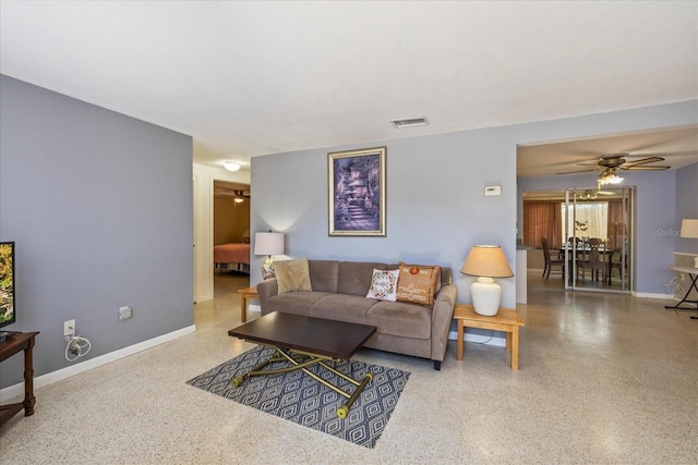 living area featuring baseboards, ceiling fan, visible vents, and speckled floor
