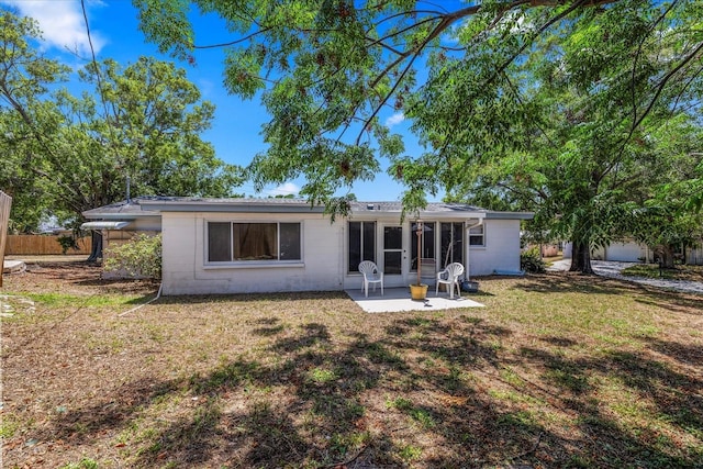 back of house featuring concrete block siding, a sunroom, a lawn, and a patio area