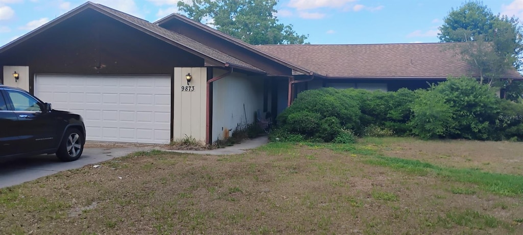 single story home featuring a garage, a front lawn, concrete driveway, and roof with shingles