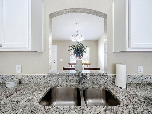 1639 Saddlehorn Dr, Lakeland, FL 33810 - kitchen with white cabinets, hanging light fixtures, light stone counters, a sink, and a chandelier