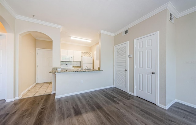 kitchen with white appliances, arched walkways, dark wood finished floors, white cabinetry, and visible vents