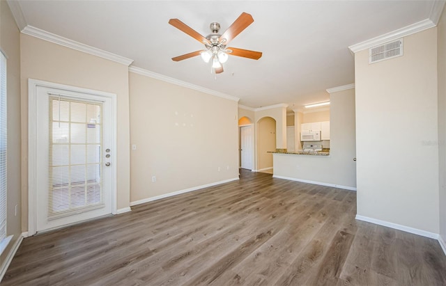 unfurnished living room featuring crown molding, arched walkways, a ceiling fan, wood finished floors, and visible vents