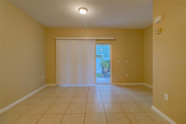 spare room featuring a textured ceiling, baseboards, and light tile patterned floors