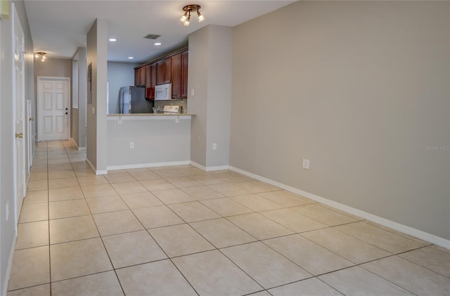 kitchen featuring visible vents, light countertops, light tile patterned floors, freestanding refrigerator, and white microwave