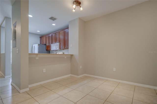 kitchen with light tile patterned flooring, white appliances, light countertops, a kitchen bar, and visible vents