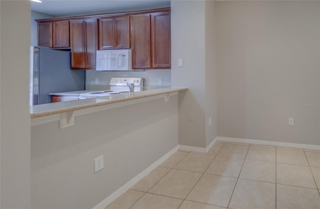 kitchen with baseboards, light countertops, a breakfast bar, and white appliances