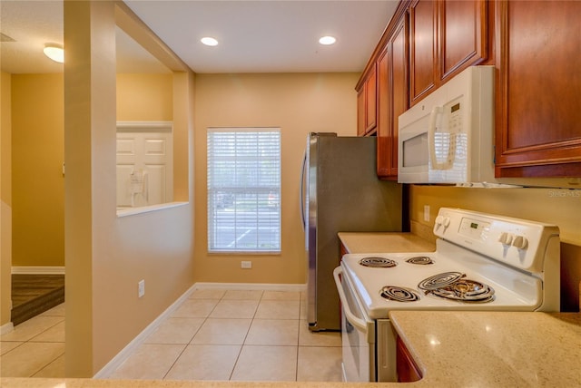 kitchen with brown cabinetry, light tile patterned flooring, white appliances, baseboards, and light stone counters