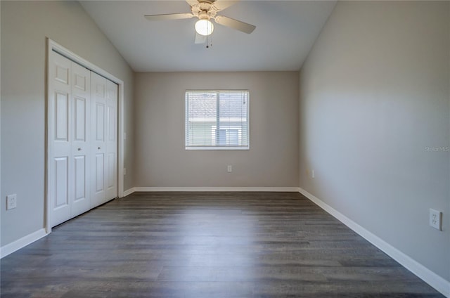 unfurnished bedroom with baseboards, a closet, dark wood-style flooring, and lofted ceiling