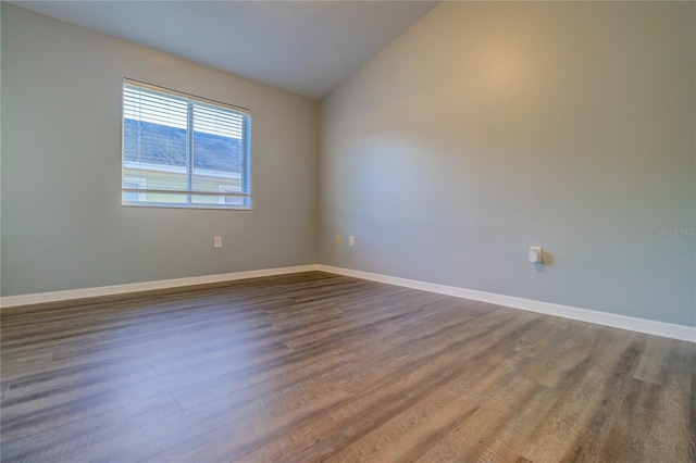 spare room featuring baseboards, vaulted ceiling, and dark wood-style floors
