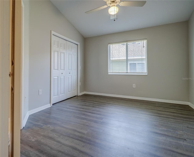 unfurnished bedroom featuring baseboards, vaulted ceiling, dark wood finished floors, and a closet