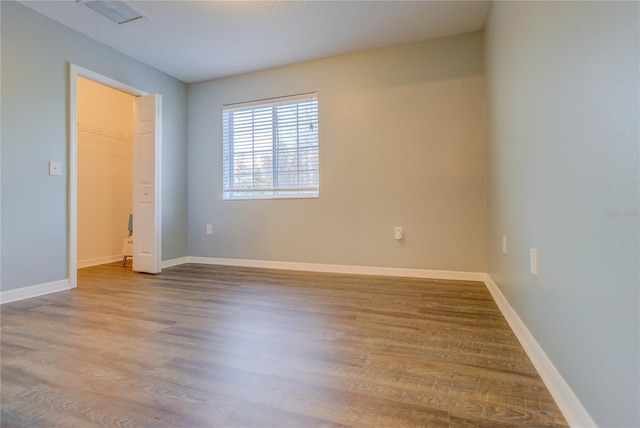 unfurnished bedroom with a spacious closet, baseboards, wood finished floors, and visible vents