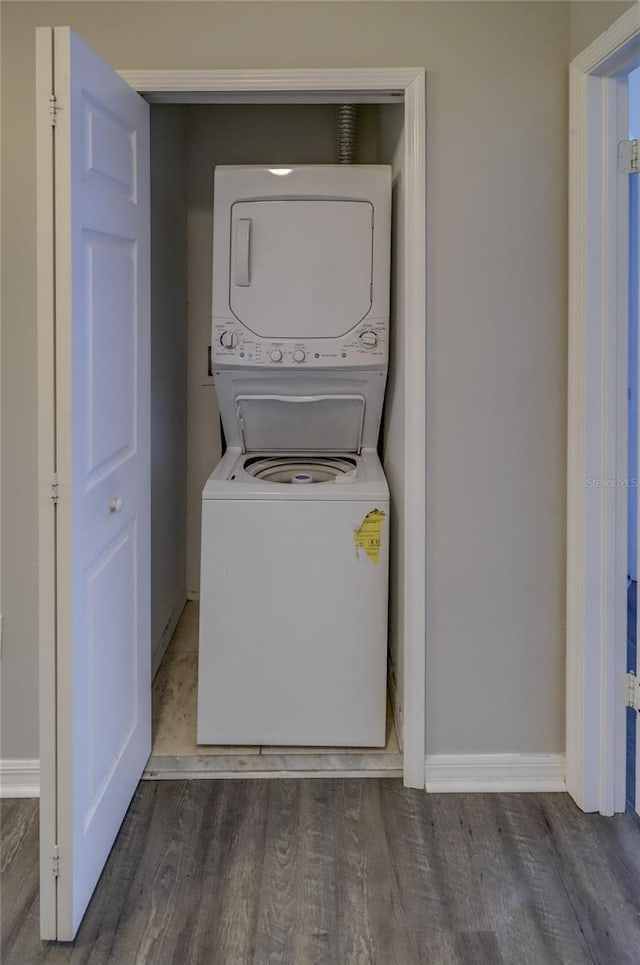 laundry area with baseboards, laundry area, stacked washer and dryer, and wood finished floors