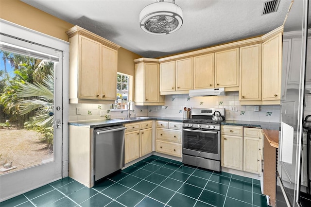 kitchen with appliances with stainless steel finishes, light brown cabinets, decorative backsplash, and under cabinet range hood