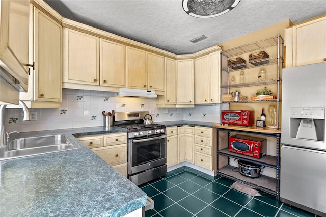 kitchen featuring a sink, stainless steel gas range, dark tile patterned floors, under cabinet range hood, and refrigerator with ice dispenser