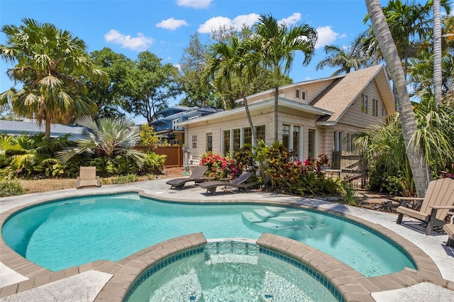 view of pool with a patio area, fence, and a pool with connected hot tub