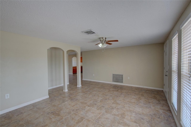 unfurnished room featuring arched walkways, a ceiling fan, a textured ceiling, and visible vents