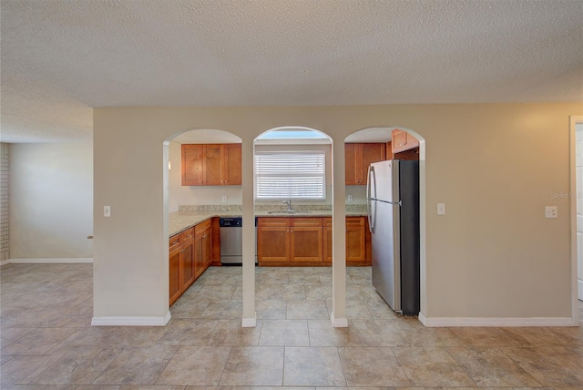 kitchen with arched walkways, a textured ceiling, appliances with stainless steel finishes, and light stone countertops