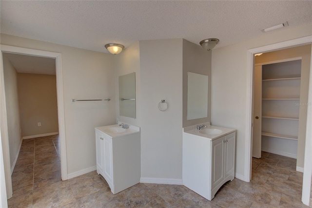 bathroom featuring a textured ceiling, two vanities, and a sink