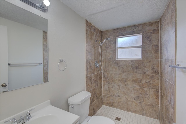 full bath with vanity, a tile shower, toilet, and a textured ceiling