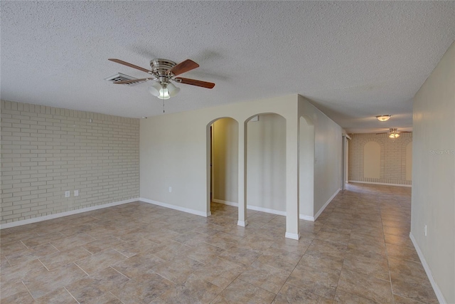 spare room with brick wall, baseboards, ceiling fan, a textured ceiling, and arched walkways