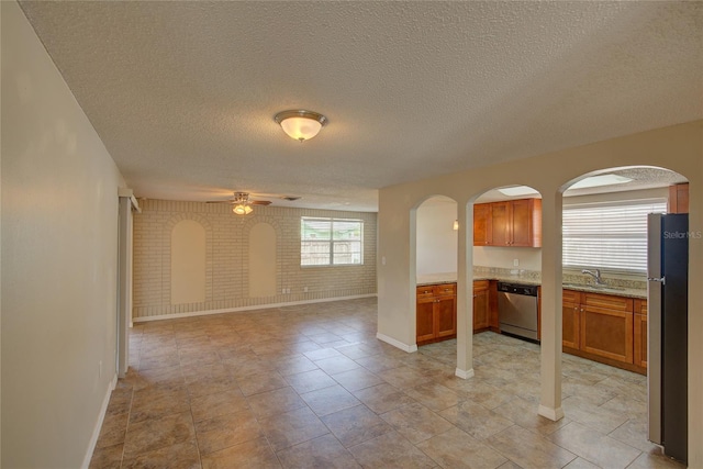 unfurnished living room with ceiling fan, a sink, arched walkways, a textured ceiling, and baseboards