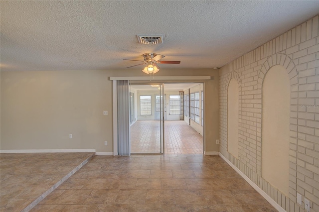 spare room with a textured ceiling, brick wall, a ceiling fan, baseboards, and visible vents