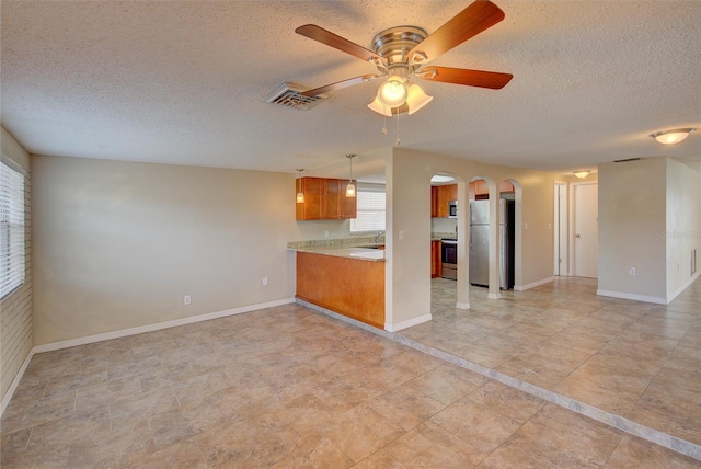 kitchen featuring brown cabinetry, a textured ceiling, appliances with stainless steel finishes, arched walkways, and open floor plan