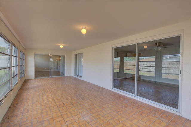 unfurnished sunroom featuring a ceiling fan, brick patterned floor, and a healthy amount of sunlight