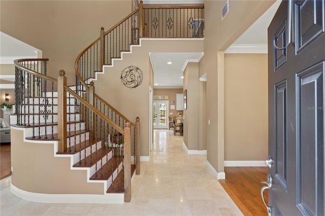 foyer entrance with stairway, baseboards, ornamental molding, and a high ceiling