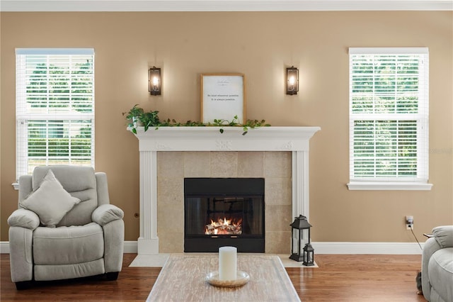 living area with a tiled fireplace, baseboards, wood finished floors, and a healthy amount of sunlight