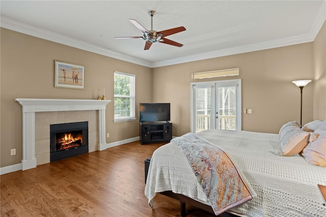 bedroom featuring ceiling fan, access to exterior, a tile fireplace, wood finished floors, and ornamental molding