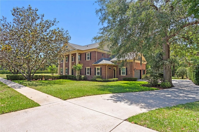 greek revival house featuring brick siding, a garage, driveway, and a front yard