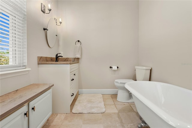 full bath featuring toilet, a freestanding tub, baseboards, and vanity