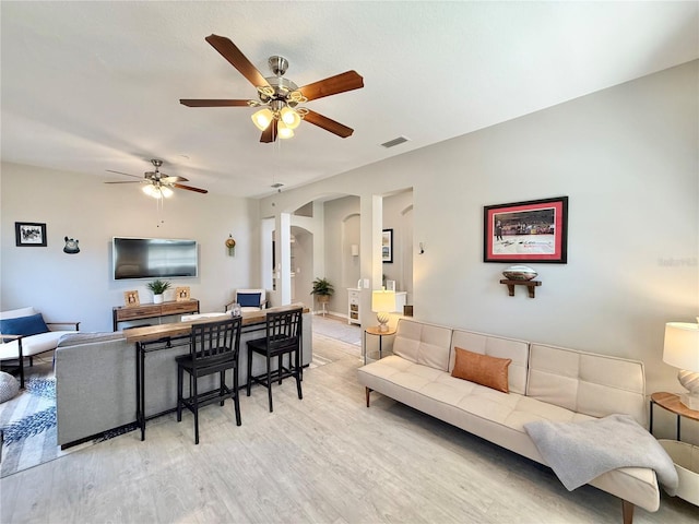 living room featuring arched walkways, ceiling fan, visible vents, and light wood-style flooring
