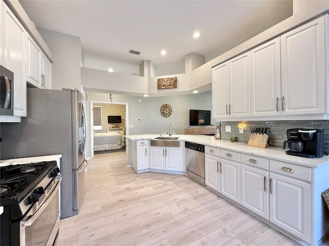 kitchen with a peninsula, white cabinetry, tasteful backsplash, a sink, and stainless steel appliances