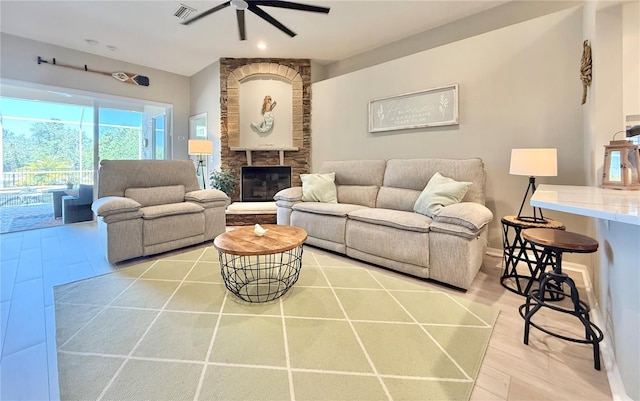 living room featuring a stone fireplace, a ceiling fan, recessed lighting, wood finished floors, and visible vents
