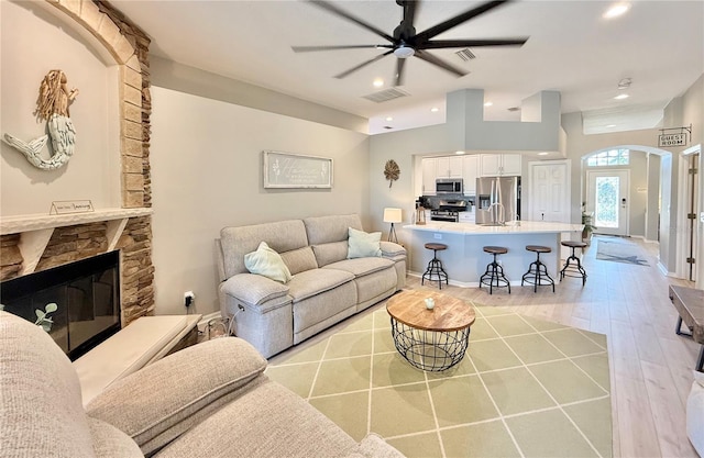 living room featuring visible vents, wood finished floors, a stone fireplace, ceiling fan, and arched walkways