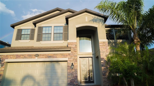 view of front of home with a garage, stucco siding, and stone siding