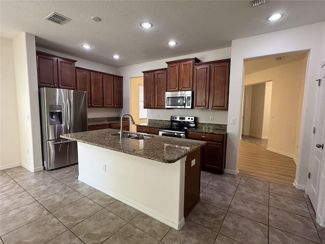2731 Hampton Green Ln, Brandon, FL 33511 - kitchen featuring appliances with stainless steel finishes, an island with sink, dark stone counters, light tile patterned flooring, and a textured ceiling