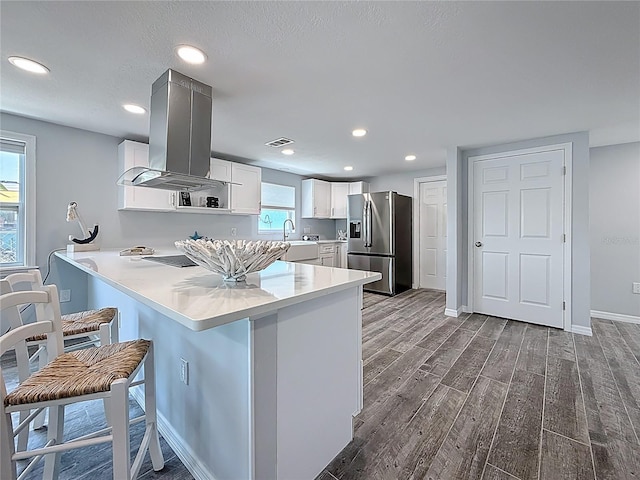 kitchen featuring visible vents, wood tiled floor, island range hood, stainless steel refrigerator with ice dispenser, and a sink