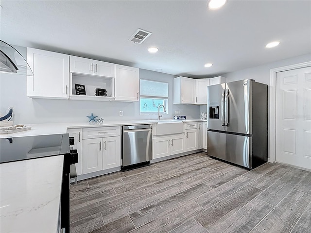 kitchen featuring visible vents, a sink, light wood finished floors, stainless steel appliances, and white cabinetry