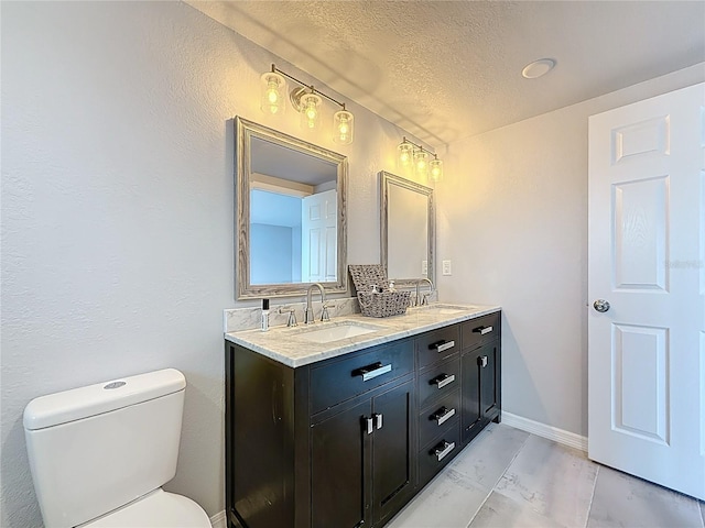 bathroom with a sink, a textured ceiling, toilet, and double vanity